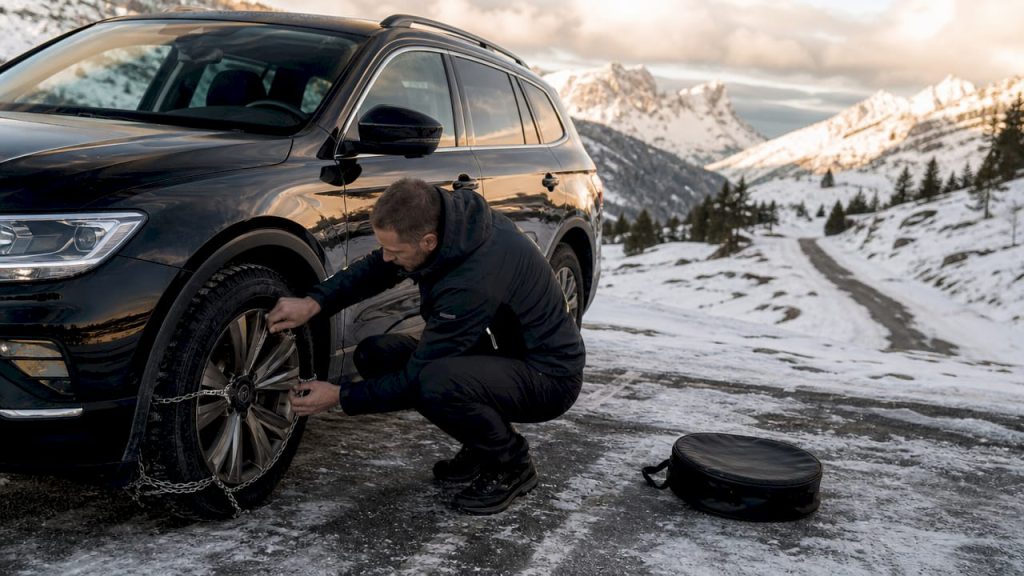 Un conducteur vérifie l’état de ses pneus neige avant de prendre la route en montagne.